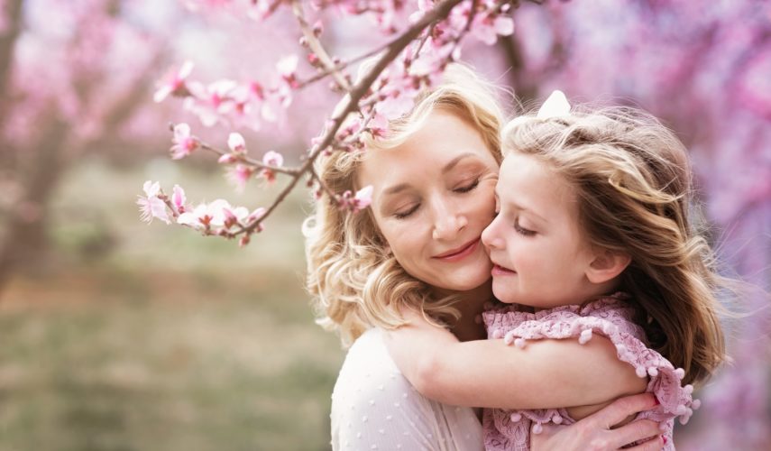 a mother hugging her daughter in front of a tree with pink flowers